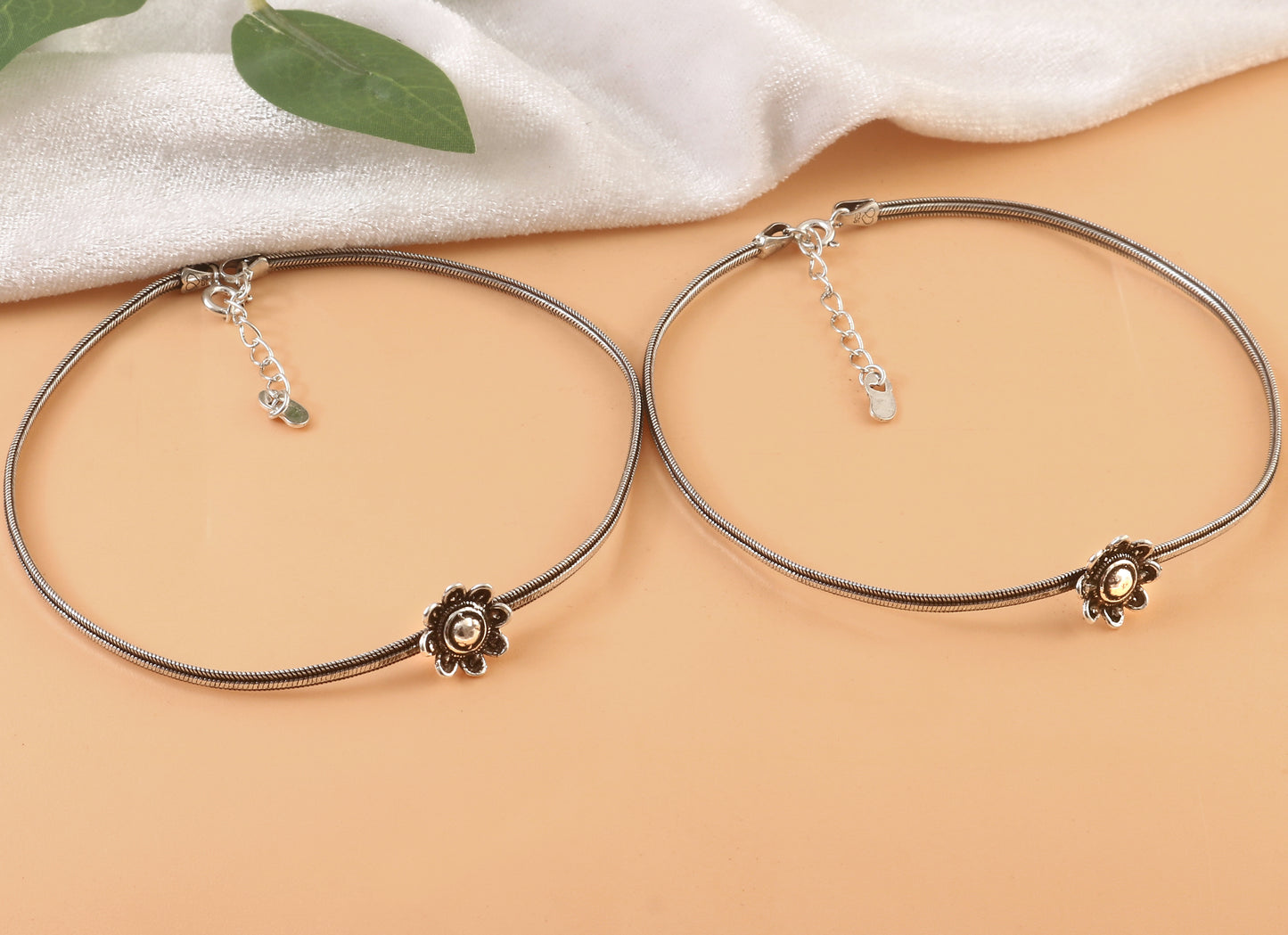 Two silver bracelets with floral ends on a beige surface