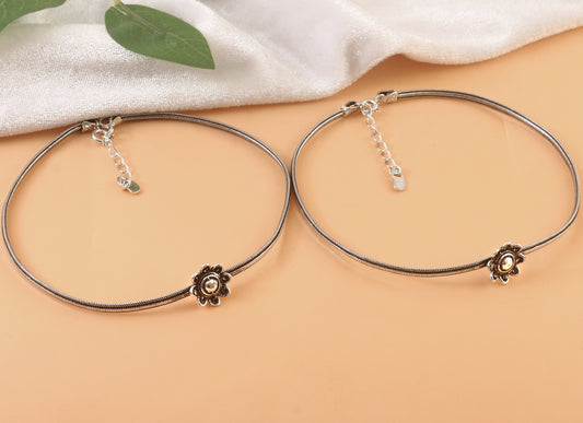 Two silver bracelets with floral ends on a beige surface